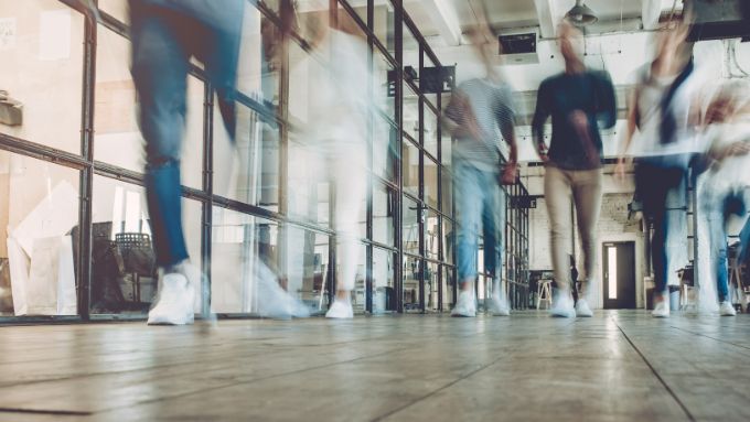 Innenliegende Glasbürowand an der Männer mit Sneakers und Jeans vorbeigehen